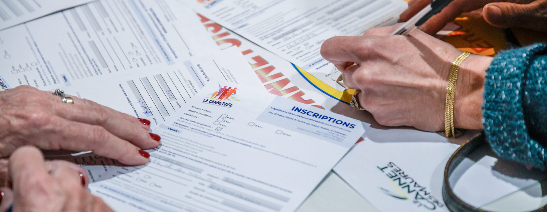 formulaires d'inscriptions éparpillés sur une table et mains remplissant les formulaires